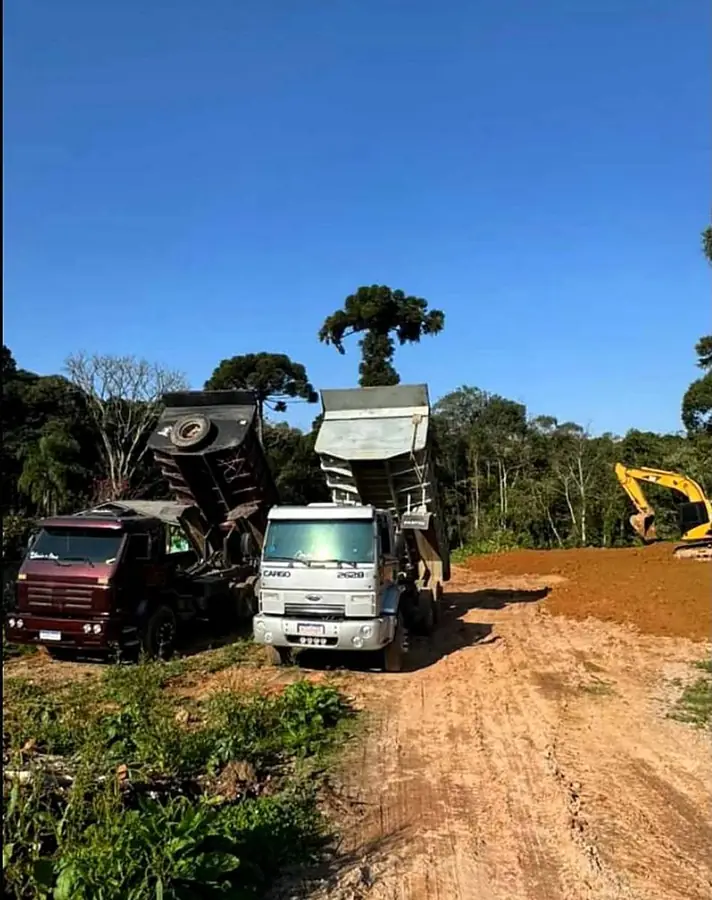 Caminhões caçamba descarregando terra e escavadeira em terraplenagem de loteamento